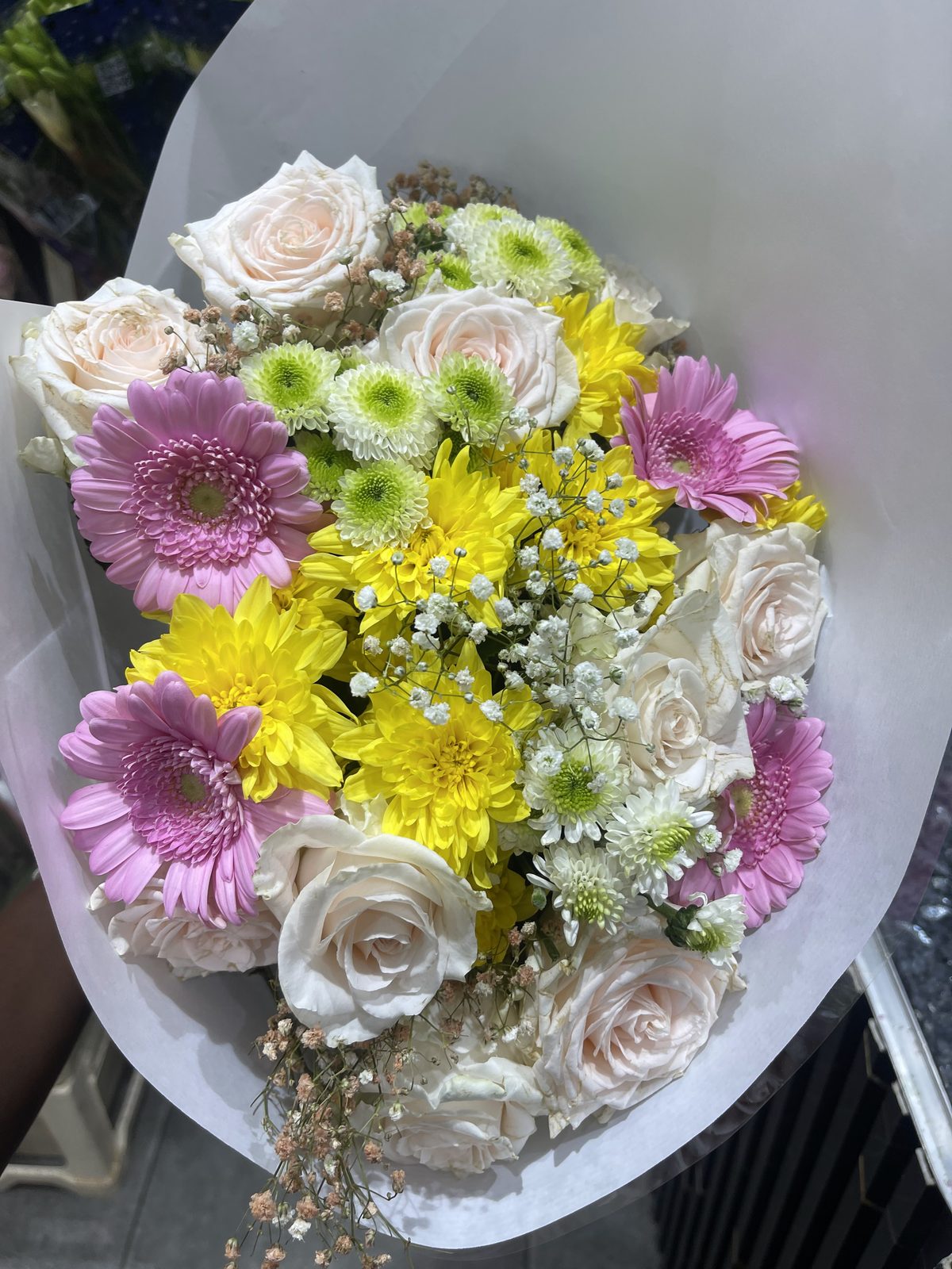 Bouquet de roses, gerberas et chrysanthèmes mauves et jaunes dans un papier blanc